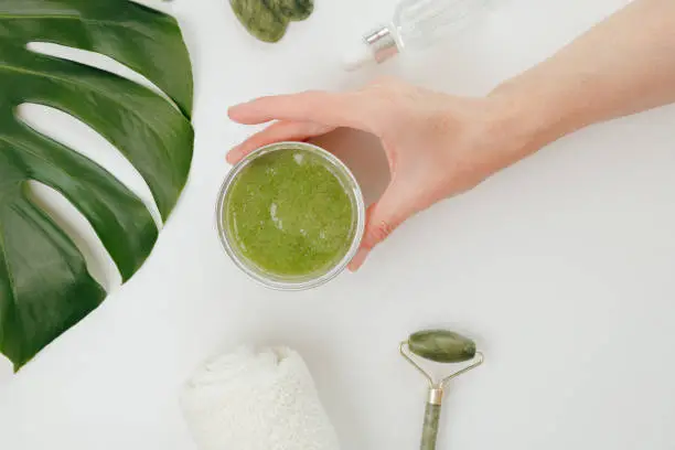 Photo of Woman Taking Jar with Cosmetics Green Natural Scrub, white background, top view