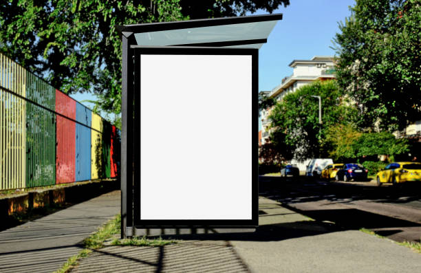bus shelter with lightbox. blank white billboard ad panel at busstop. background for mockup bus shelter at a bus stop. empty white poster ad. advertising display panel and light box. mockup template. glass and aluminum frame. urban street perspective. green background with trees and parked cars. bus shelter stock pictures, royalty-free photos & images