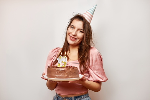 The girl is holding a festive cake with a candle in the form of the number 19. The concept of a birthday celebration.