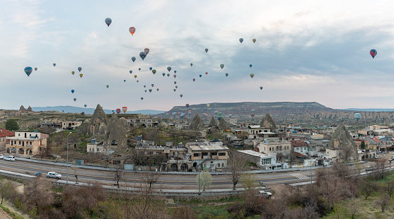 A picture of hot air balloons flying over the Goreme Historical National Park and the town of Goreme at sunrise.