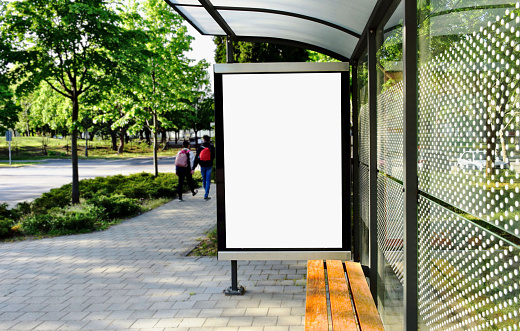 image composite of bus shelter at a bus stop. empty white poster ad and advertising display glass and light box. aluminum frame structure. outdoor street perspective, green background with trees.