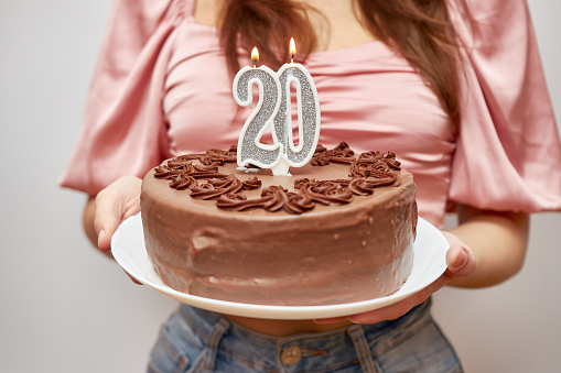 The girl is holding a festive cake with a candle in the form of the number 20. The concept of a birthday celebration.