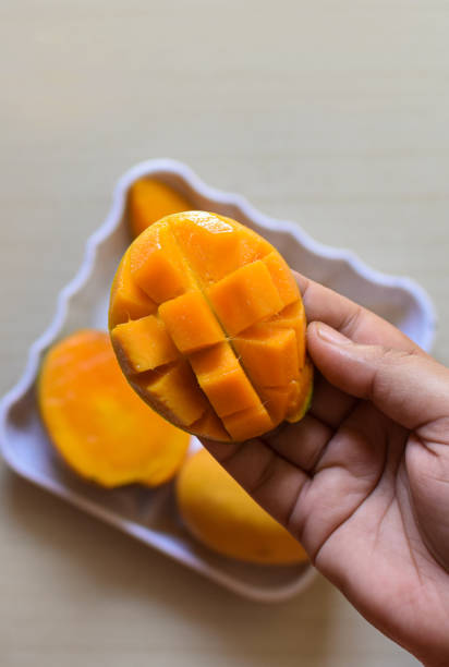 отлично подойдет ломтик манго, нарезанный кубиками. жен�ские руки держат свежее сочное манго. как разрезать манго учебник - serving food fruit salad human hand стоковые фото и изображения