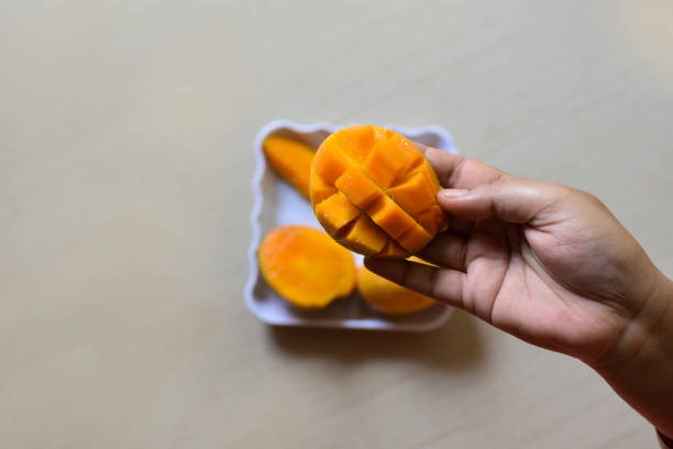 отлично подойдет ломтик манго, нарезанный кубиками. женские руки держат свежее сочное манго. как разрезать манго учебник - serving food fruit salad human hand стоковые фото и изображения