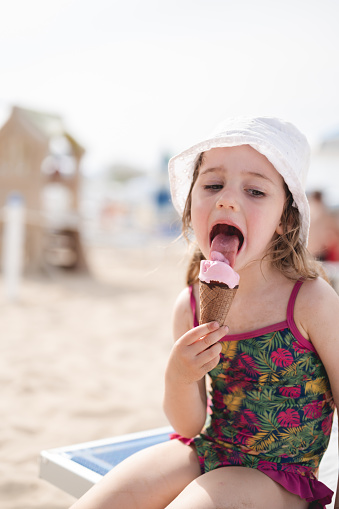 little girl licking ice cream on a beach.