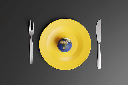 The earth on a yellow dining plate with knife and fork on black background. Illustration of the concept that humans consuming resources of the blue planet
