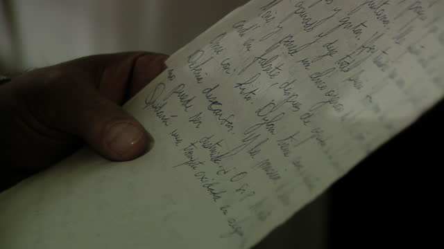 Hands of a Man Reading A Sheet of Paper in Dark Room. Close Up.