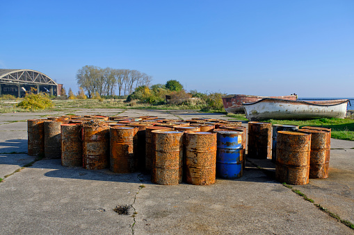 Rusty fuel barrels shore against background old hangar and boats