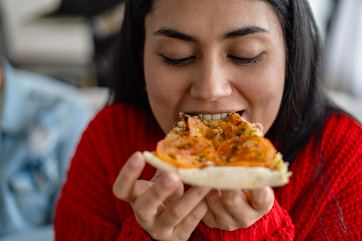 Portrait of a Latina woman eating pizza in her living room.