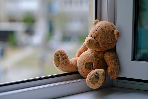 Bear childrens soft toy sitting edge an open window.Concept accidents with children