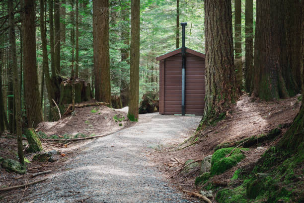 Small wooden building known as outhouse, latrine or drop toilet with walking way. Camping or cottage in the wilderness. North Vancouver, BC, Canada. Selective focus.