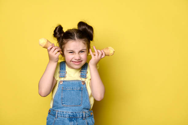 istock Mischievous naughty little kid girl making faces, grimacing, posing with ice cream waffle cones over yellow background 1499035486