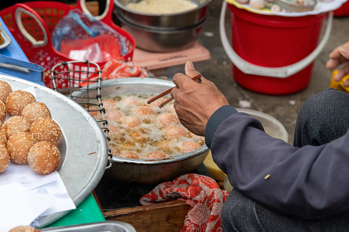 Close up of the hand above a frying pan of a man with chopsticks preparing doughy fish balls on the Bac Ha Sunday market in Vietnam