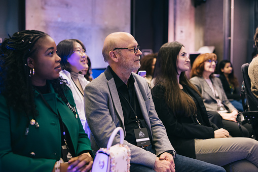 A diverse business tech audience listens intently to a startup entrepreneur on stage. Their attentive expressions and thoughtful postures reflect their respect for the speaker's expertise and their desire to gain valuable insights.
