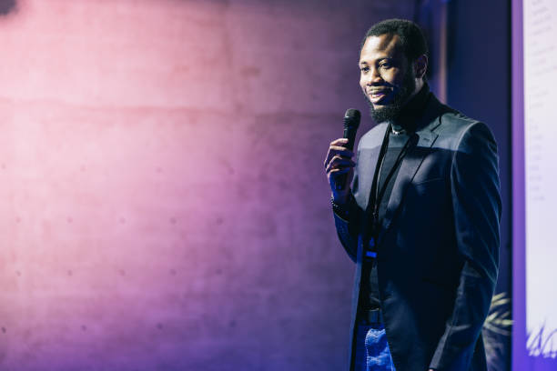 In a dynamic setting of a startup tech conference, a business entrepreneur stands before a captivated audience, delivering an inspiring presentation. Their passionate delivery and insightful perspectives resonate with the attendees.