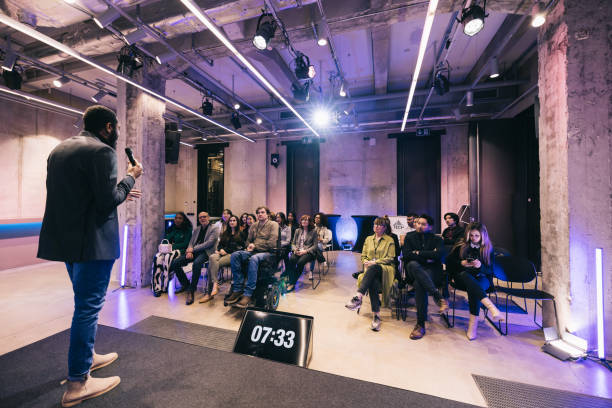 Against the backdrop of a startup tech conference, a business entrepreneur takes the stage, delivering an impactful presentation. Their confident posture and charismatic delivery hold the audience's attention.