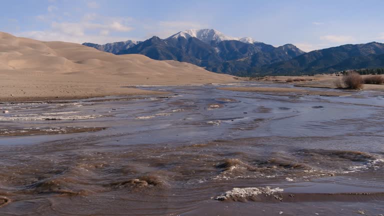 Spring at Medano Creek - Medano Creek rushing down a sandy valley at base of rolling Great Sand Dunes and snow-capped Mt. Herard on a sunny Spring morning. Great Sand Dunes National Park, Colorado, USA.