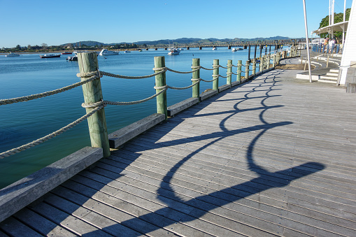Shadow patterns of rope and post bollards along Tauranga City waterfront.with harbour and blue sky background.