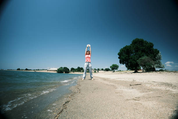 Smiling mature woman is exercising on water's edge