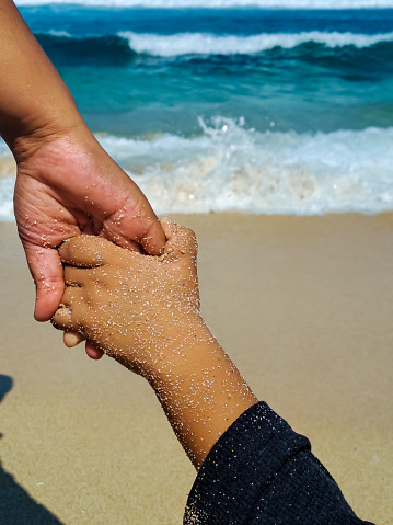Close up view of father and son holding hand on the beach. Family trust, support and care concept