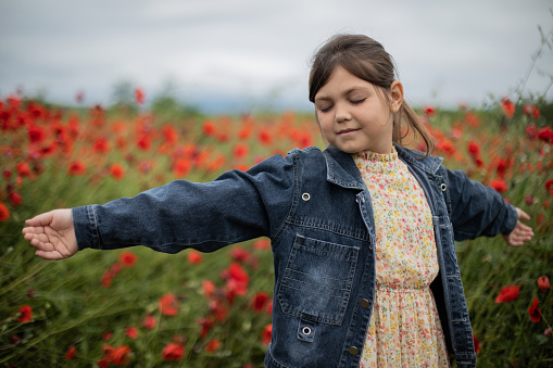 It's a spring time and young pretty little girl is spending her free time in wonderful poppy flower field. She is spreading hands with joy and enjoying in nature.