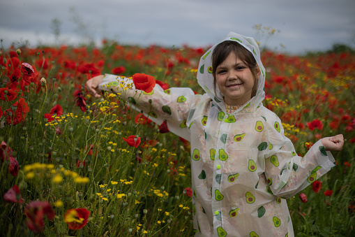 It's a rainy spring day and young pretty little girl is spending her free time in wonderful poppy flower field. She is wearing her raincoat and she is playing and enjoying in nature. She loves rain.