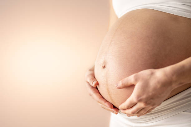 femme enceinte tenant doucement son ventre rond nu avec ses mains au cours du dernier mois de grossesse. troisième trimestre - semaine 36. gros plan. vue latérale. arrière-plan bege. prise de vue lumineuse. - table chair white curve photos et images de collection