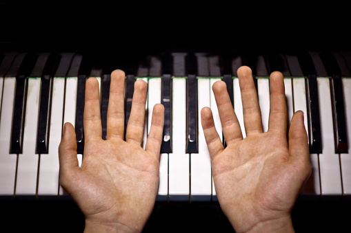 two male hands on the piano. palms lie on the keys and play the keyboard instrument in the music school. student learns to play. hands pianist. black dark background. top view.
