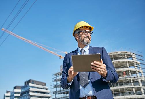 senior businessman architect wearing a protective helmet using a tablet on the construction site