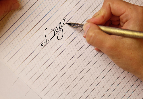 female hand writes with the inky pen the word logo on a white paper sheet with stripes. stationery on desk close up top view. spelling lessons and caligraphy exercises. Template, layout, background.