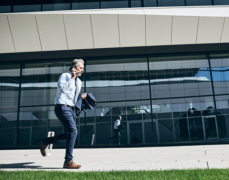 senior businessman in a rush  running and using a phone smartphone outdoors