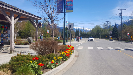 Pemberton, British Columbia, Canada- April 27,2023:  Small business,people walking. Springtime with tulips planted. Beautiful clear day with mountains and snow.