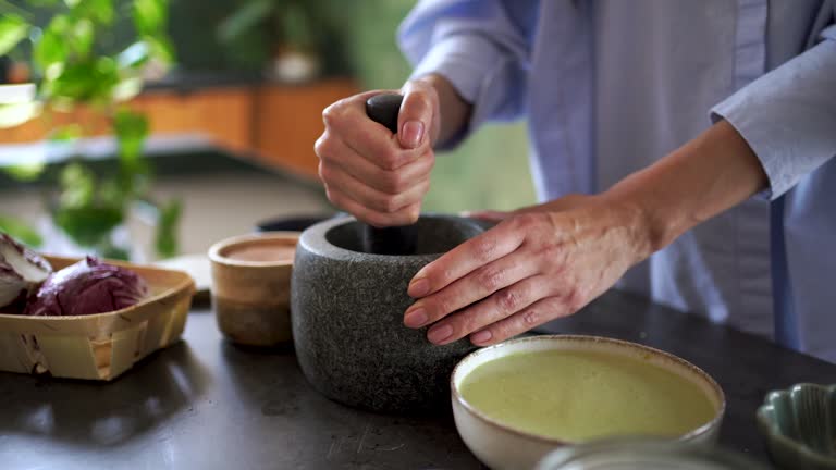 Woman grinding ingredients with mortar and pestle in kitchen