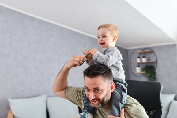 istock Cute Smiling Baby Boy Stealing Father's Eyeglasses While Getting Carried On Shoulders 1499060016