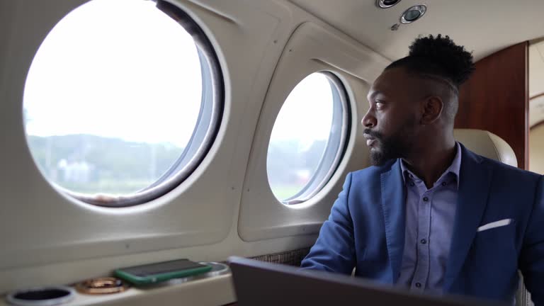 Mid adult businessman looking through window contemplating while use laptop in a corporate jet