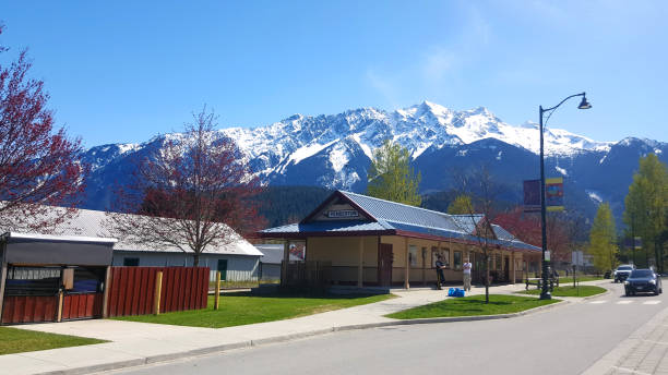 Street Scene Pemberton British Columbia With Old Train Station And Mt Currie Pemberton, British Columbia, Canada- April 27,2023: Springtime scenic of Old train station now a small business.  Two men talking. Large snow capped mountain range in background. Quiet small town. pemberton town stock pictures, royalty-free photos & images