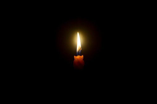 A single burning candle flame or light is glowing spiral orange candle on black or dark background on table in church for Christmas, funeral or memorial service with copy space.