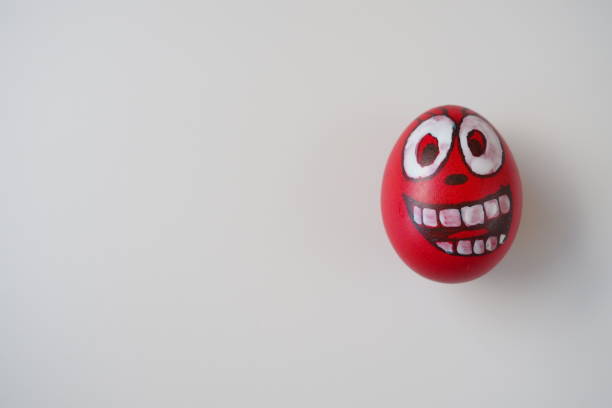 Easter egg painted red, white and black with a cheerful toothy face. Boiled chicken dyed egg with red shell. White background. Big eyes, white teeth on the fun face. Copy space.