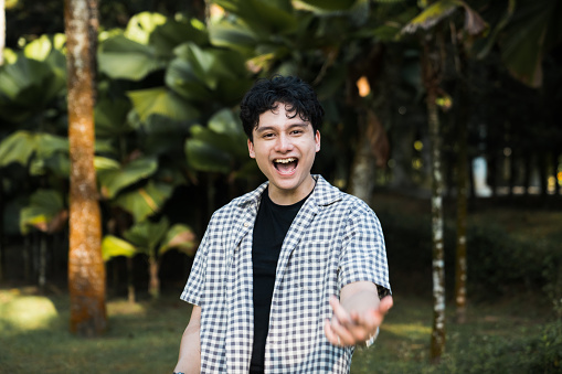 Portrait of a young Asian man laughing and posing  at camera with nature in background.