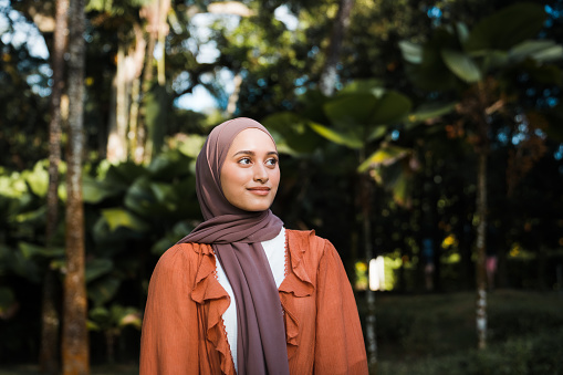 Portrait of a confident Muslim Asian woman looking away with nature in background.