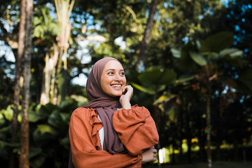 Portrait of a confident smiling Muslim Asian woman looking away with nature in background.