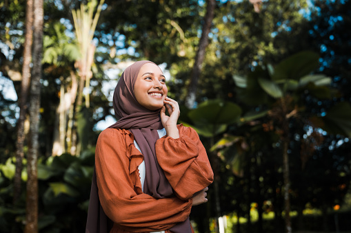 Portrait of a confident smiling Muslim Asian woman looking away with nature in background