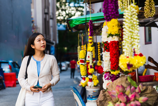 Asian woman looking at the hanged floral garlands in city.