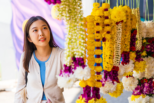 Asian woman looking for the hanged floral garlands in city.