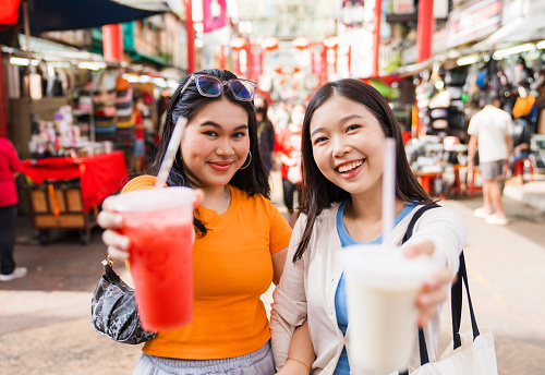 Asian girls enjoying drinks while walking out in the city, spending time together.