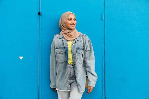 Muslim Asian woman wearing headscarf isolated against blue background looking away.