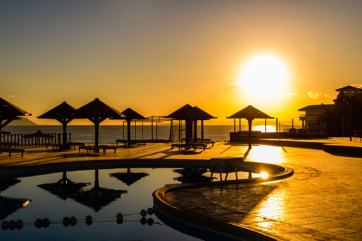 Young blonde woman walking by swimming pool at tropical beach with palm trees at scenic sunset, Zanzibar, Tanzania