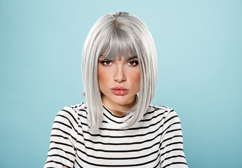 Serious young female model with gray hair in striped t shirt looking at camera against blue background