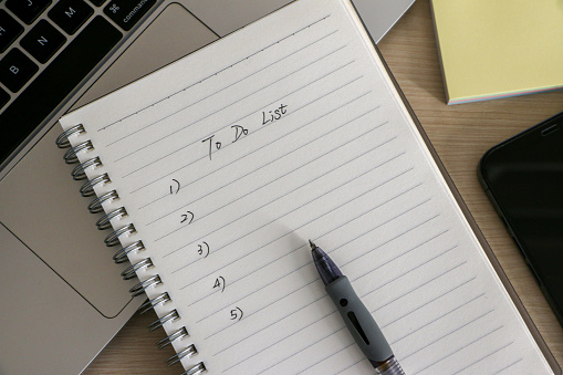 Organization and To Do List concept, workplace with notepad, ballpoint pen, some sticky notes, a laptop and smartphone, on wooden desk. Checklist for work and life.