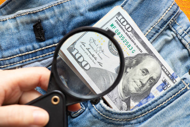 ジーンズの穴から突き出たアメリカの100ドルは、読書用の虫眼鏡で拡大された接写 - currency paper currency wealth one hundred dollar bill ストックフォトと画像